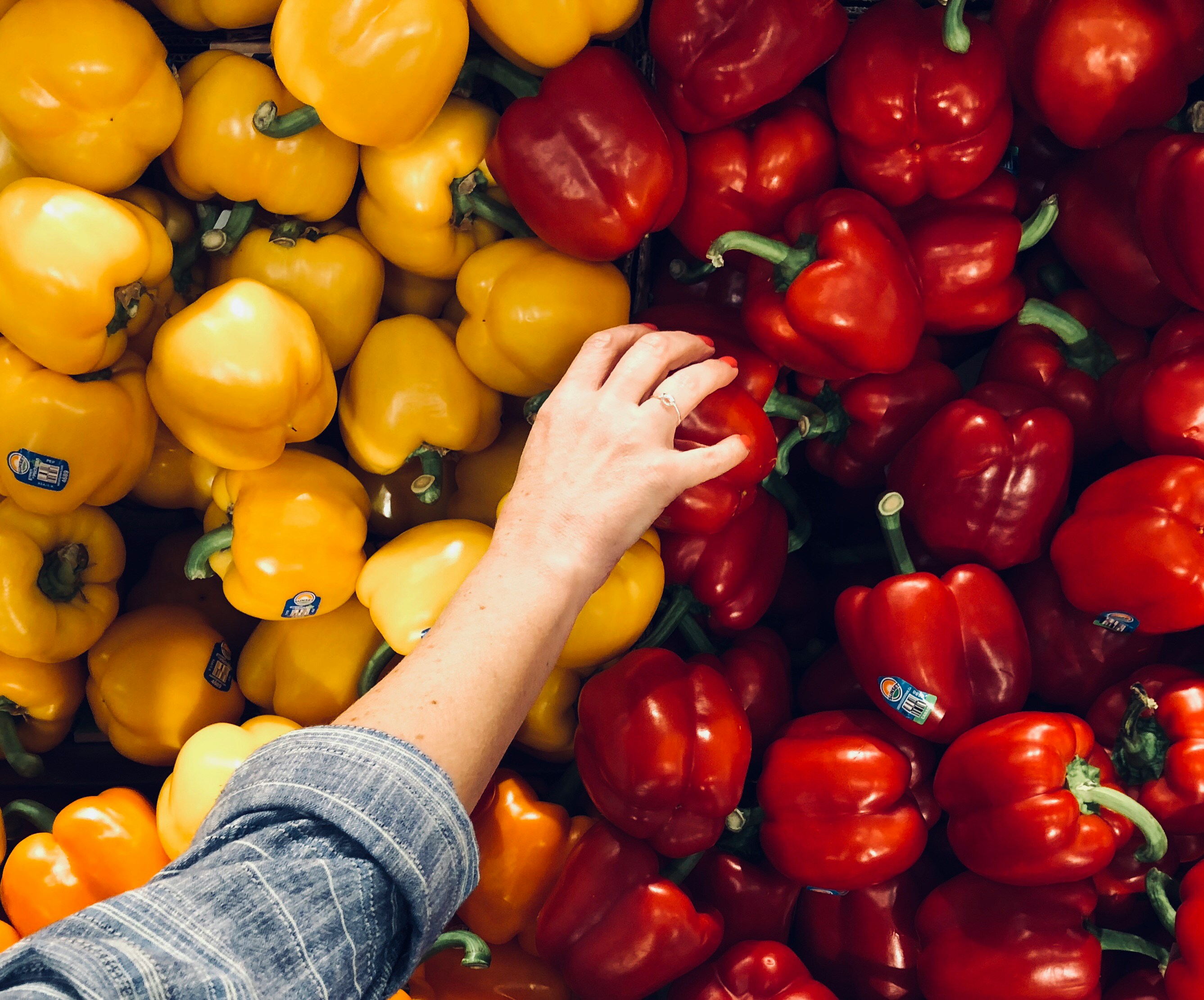 A hand reaches down into a pile of red and yellow peppers.
