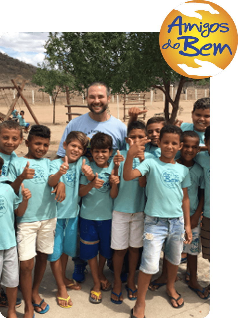 A young person with curly hair smiles at the camera while sitting in front of a laptop against a dark background.