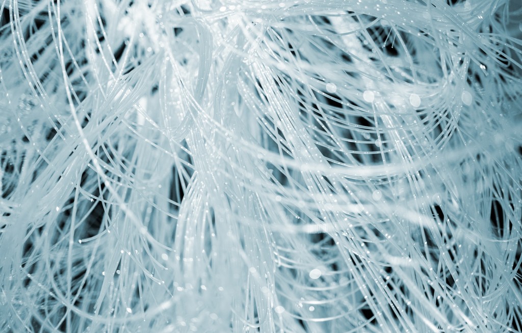 Abstract close-up of tangled, translucent white strands layered densely across the frame, with fine threads overlapping and small points of light reflecting off the surfaces, creating a soft, icy-blue, textured appearance.