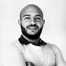 Young man in beige hoodie and cargo pants against a blue background, showcasing casual fashion style.