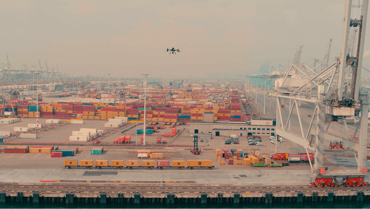 Drone die over gestapelde scheepscontainers and portaalkranen vliegt in een drukke containerhaven