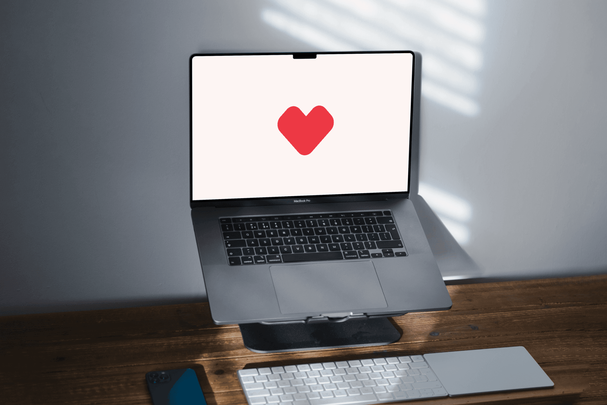 A sleek, modern laptop with a prominent heart symbol displayed on its screen sits on a wooden desk, accompanied by a wireless keyboard and mouse, with natural light casting gentle shadows across the workspace.
