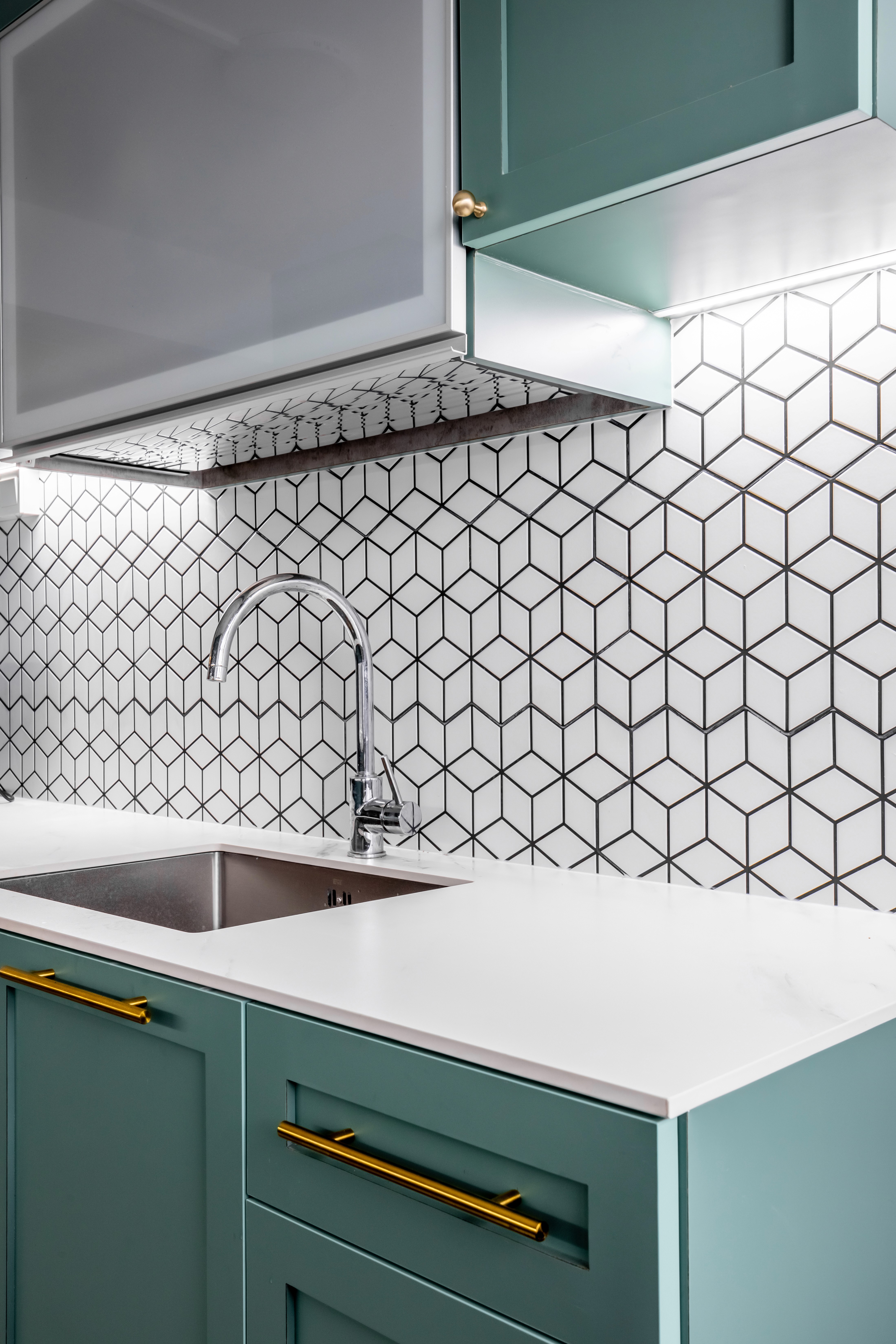 A close-up of the kitchen sink area, showcasing the chrome faucet, white quartz countertop, and cube-pattern backsplash tiles.