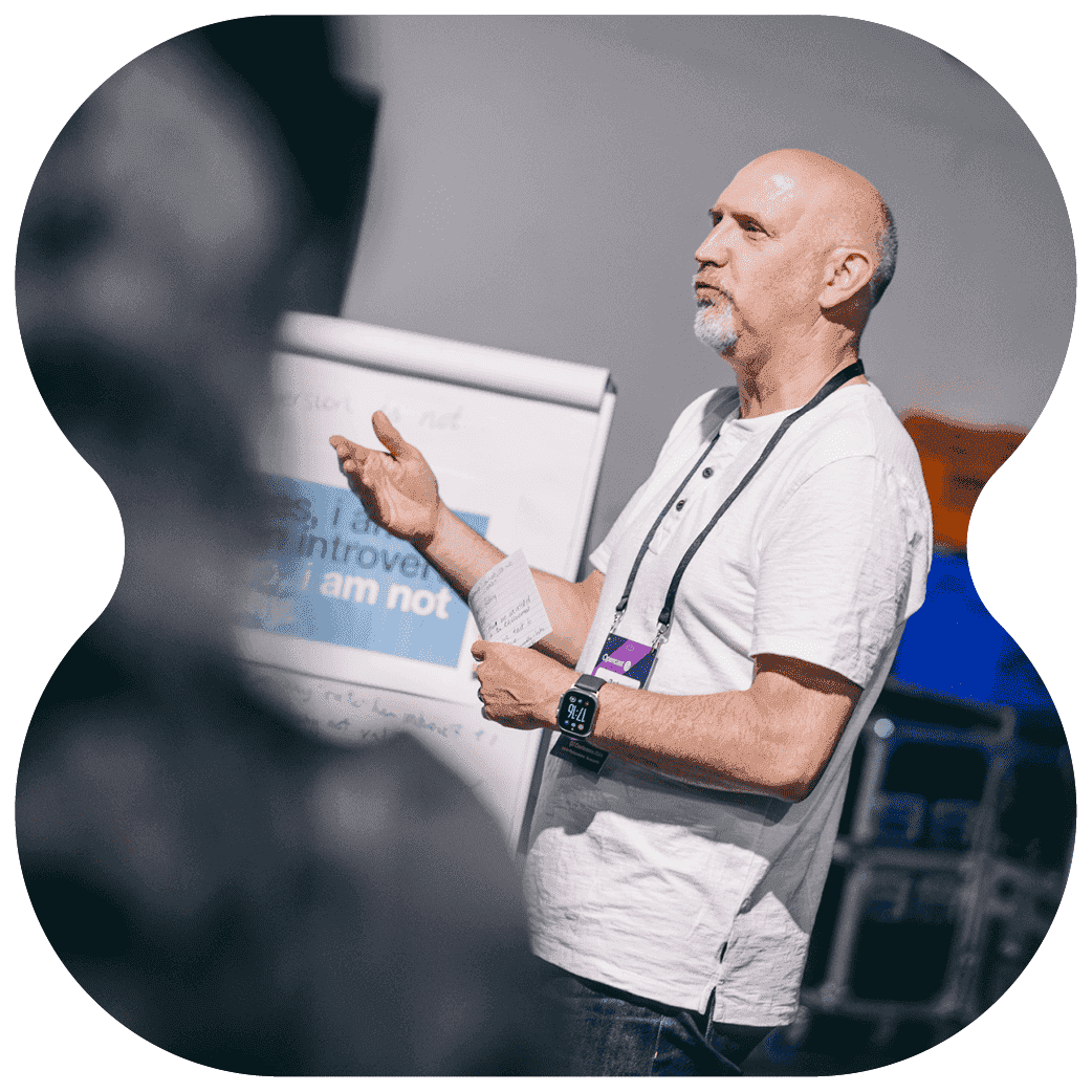 A person standing beside a flipchart and gesturing while presenting to a group.