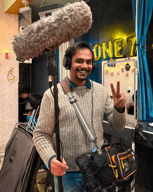 Man in a blue suit standing on a bright red geometric structure against a clear blue sky.