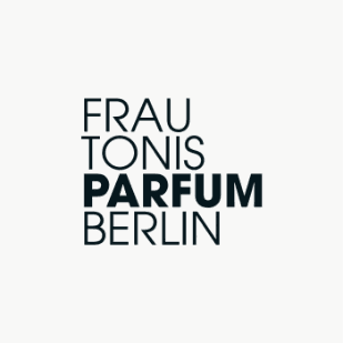 Young person with wavy hair poses confidently in sunlight against a modern building backdrop. Wears a black blazer and silver necklace, conveying elegance.