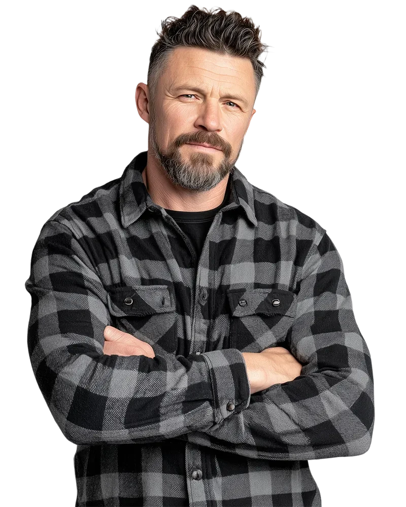 A man with a beard and neatly styled hair stands confidently with arms crossed. He wears a black and gray plaid shirt