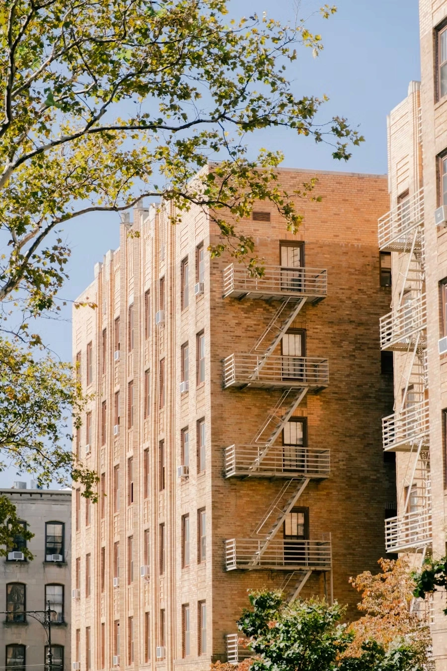 A modern building with multiple balconies, surrounded by trees and blue sky.