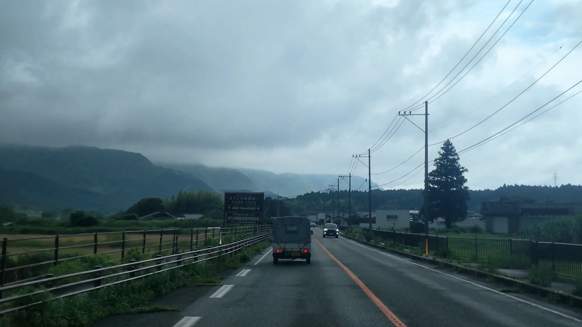 Driving a Kyushu highway toward Kurokawa Onsen, a truck ahead and hills beyond