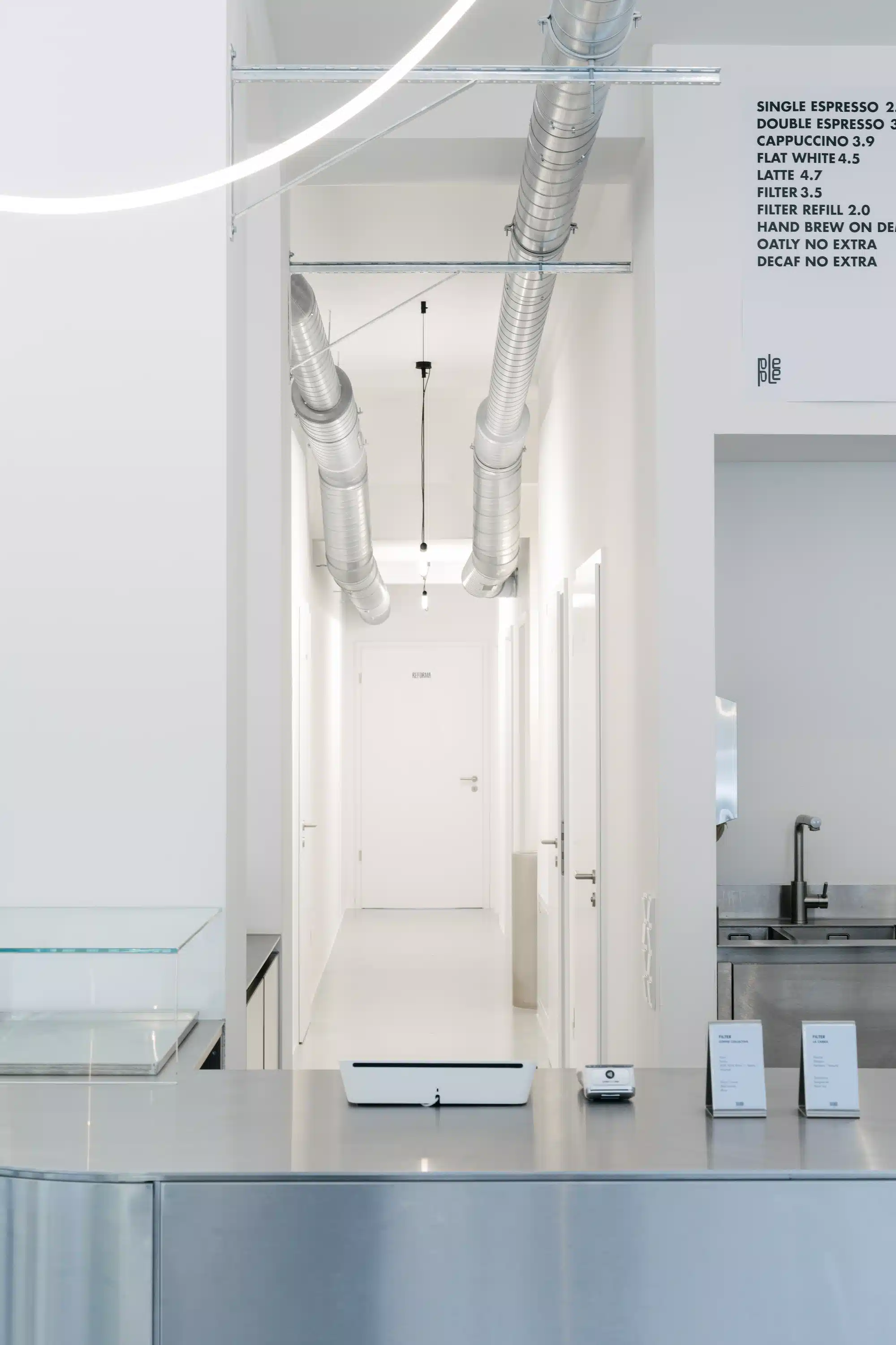 Reforma – white minimalist corridor with coffee menu on the wall, ventilation pipes and counter in the foreground