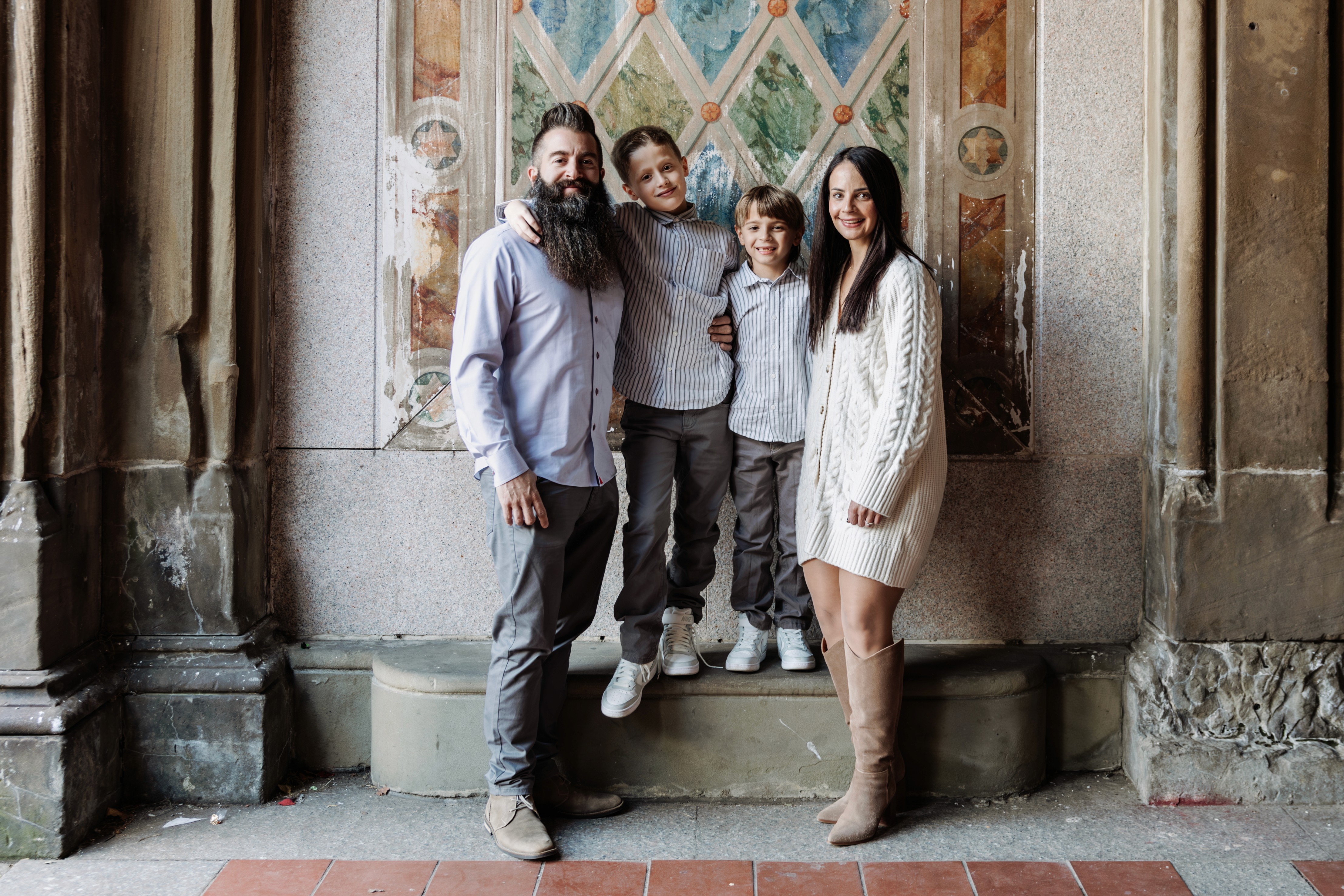 Mom, dad and their two boys all smiling at the camera at Bethesda Terrace in Central Park, NYC — a New Jersey family making memories in the city with Lizz Spano Photography, New York City family photographer.