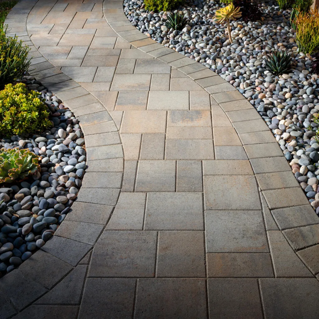 Warm rectangular paver path curving beside gray stones and garden planting.