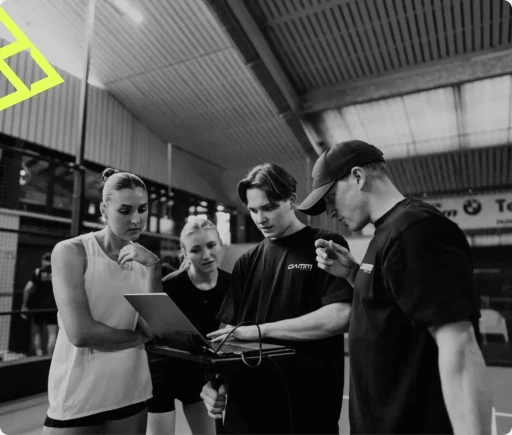 Schwarz-Weißes Behind the Scenes Bild aus einer Produktion von Damm Media in einer Tennishalle –&nbsp;dem Match Center in Filderstadt mit zwei Personen aus dem Team von Damm Media und drei gelben Dreiecken in der linken Ecke oben. 