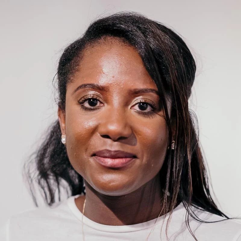 A person with long dark hair wears a white top. They are photographed against a clean, light background.