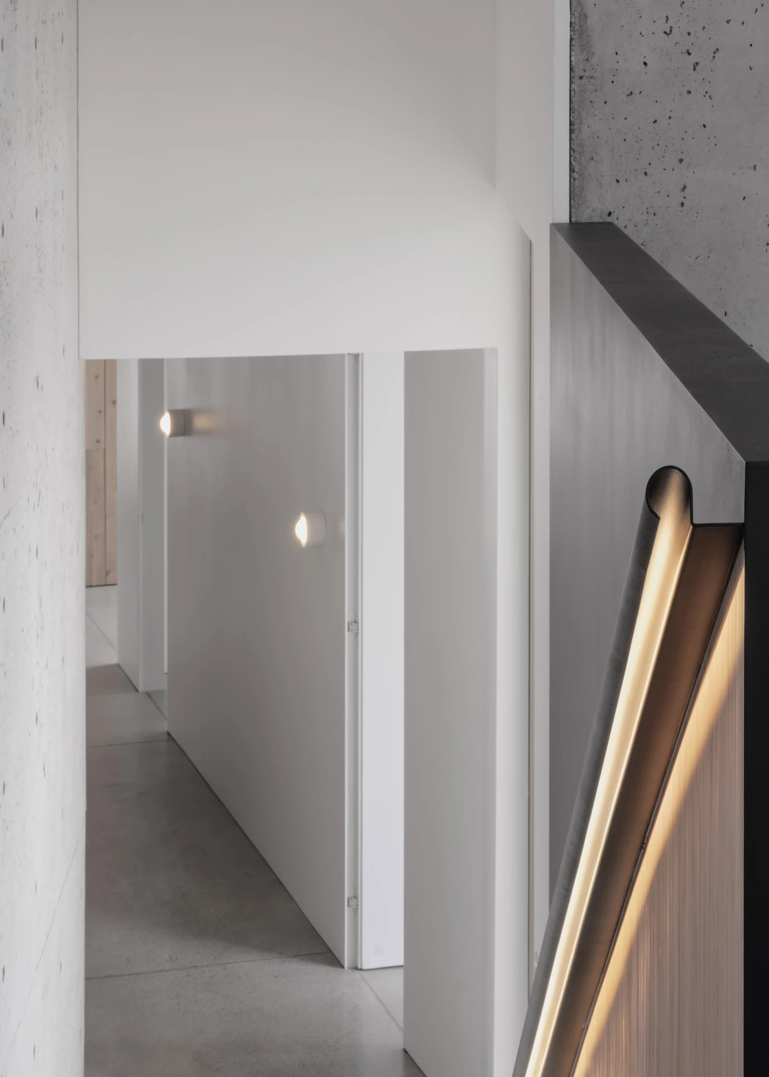 Escalier en bois clair avec garde-corps minimaliste et paroi noire, éclairé par la lumière naturelle.