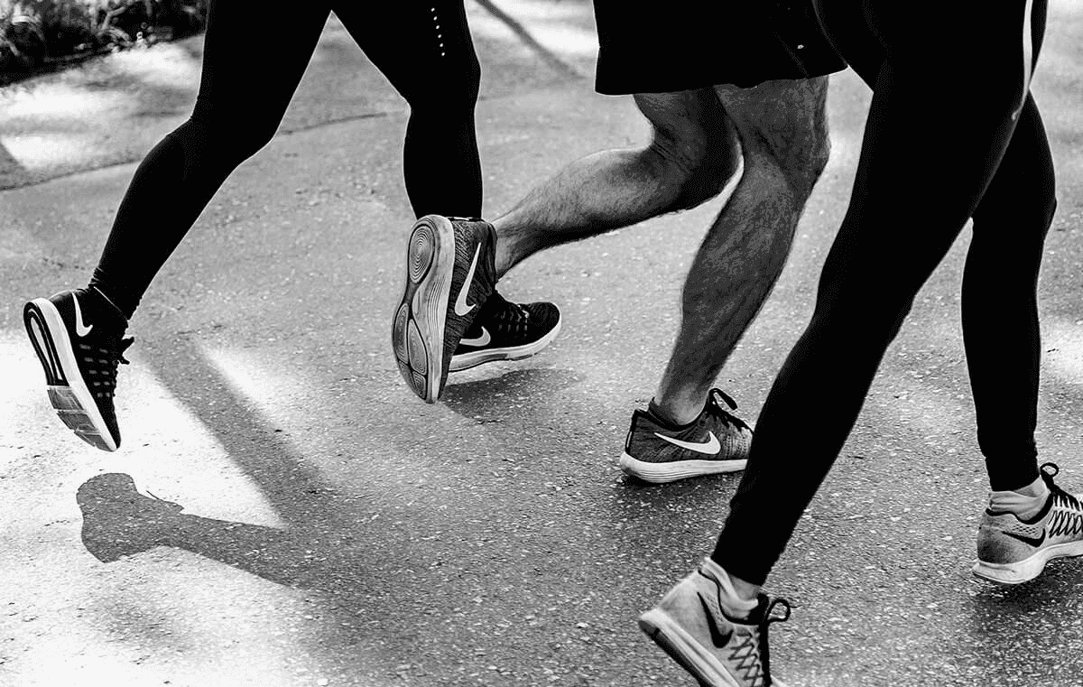 Black and white close-up of the legs and feet of three people running together on a paved path.
