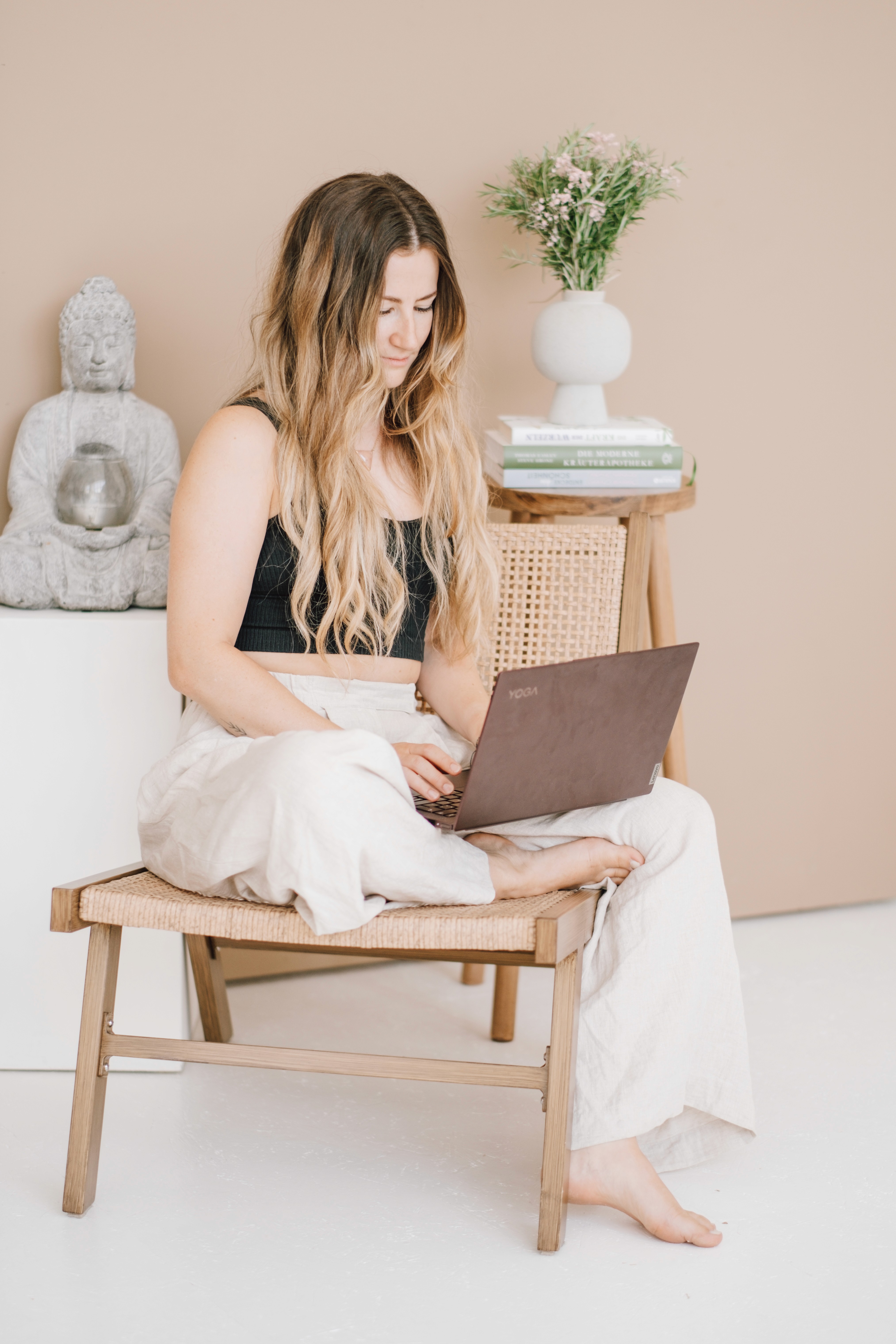 Antonia sitzt auf weißer Coach im Schneidersitz, mit dem Laptop auf dem Schoß
