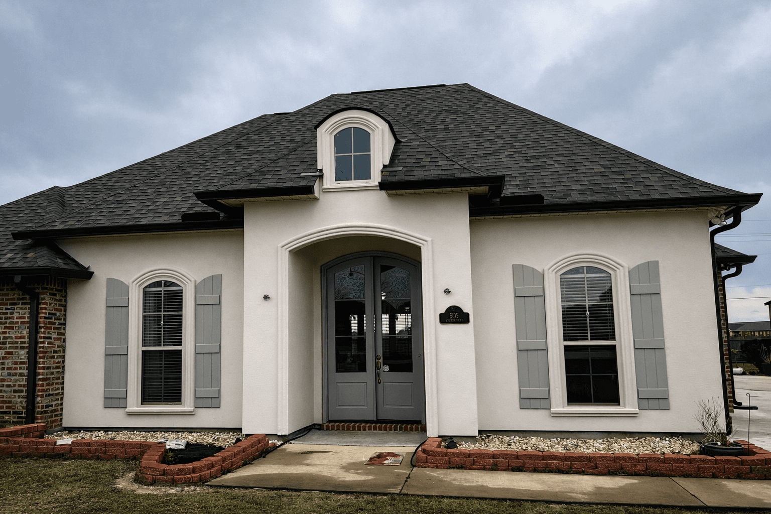 Modern glass and wood cabin with a cozy outdoor deck featuring wicker furniture, surrounded by lush green trees and a serene forest setting.