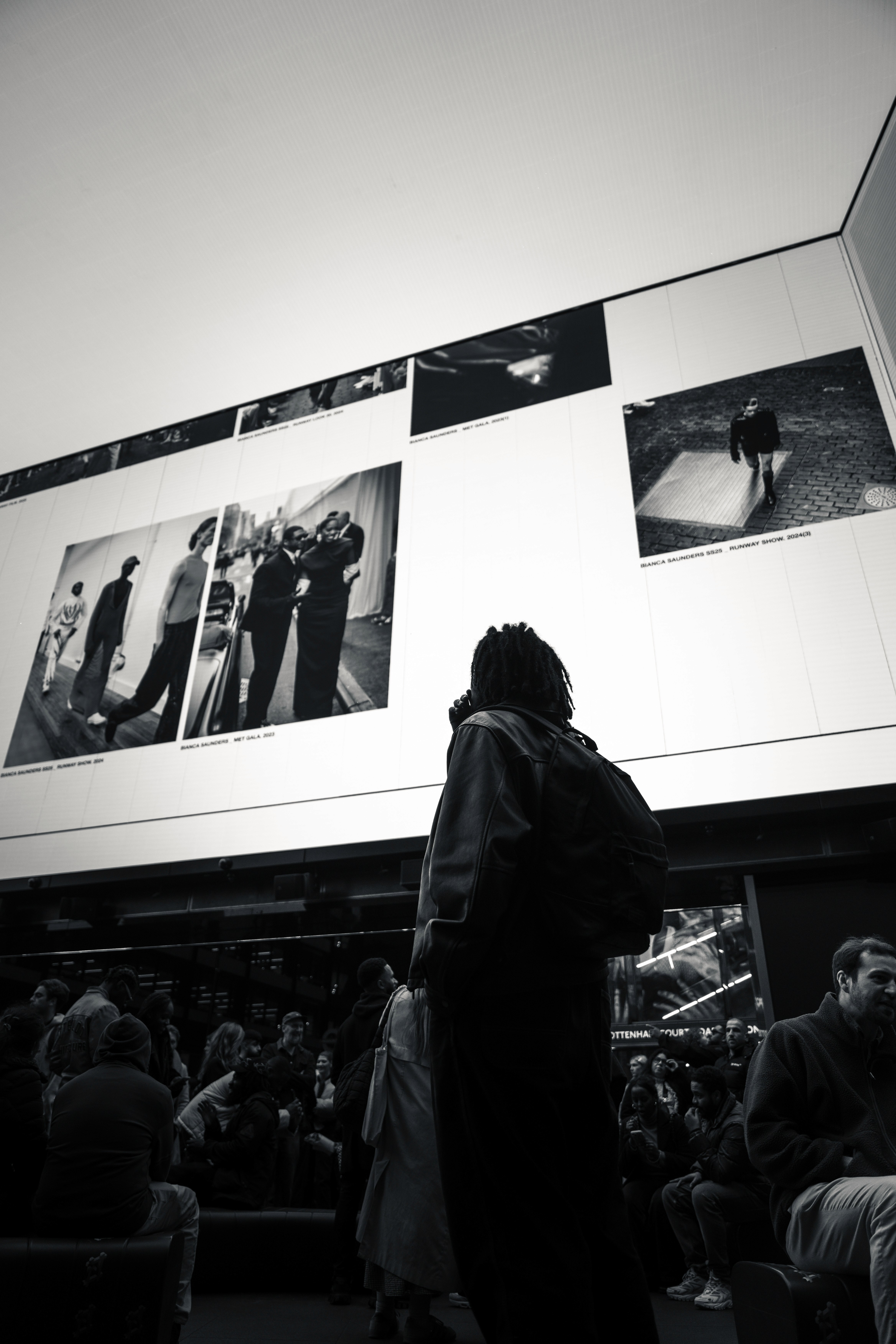 Visitor looking up at black-and-white photographs projected on the walls at Outernet London