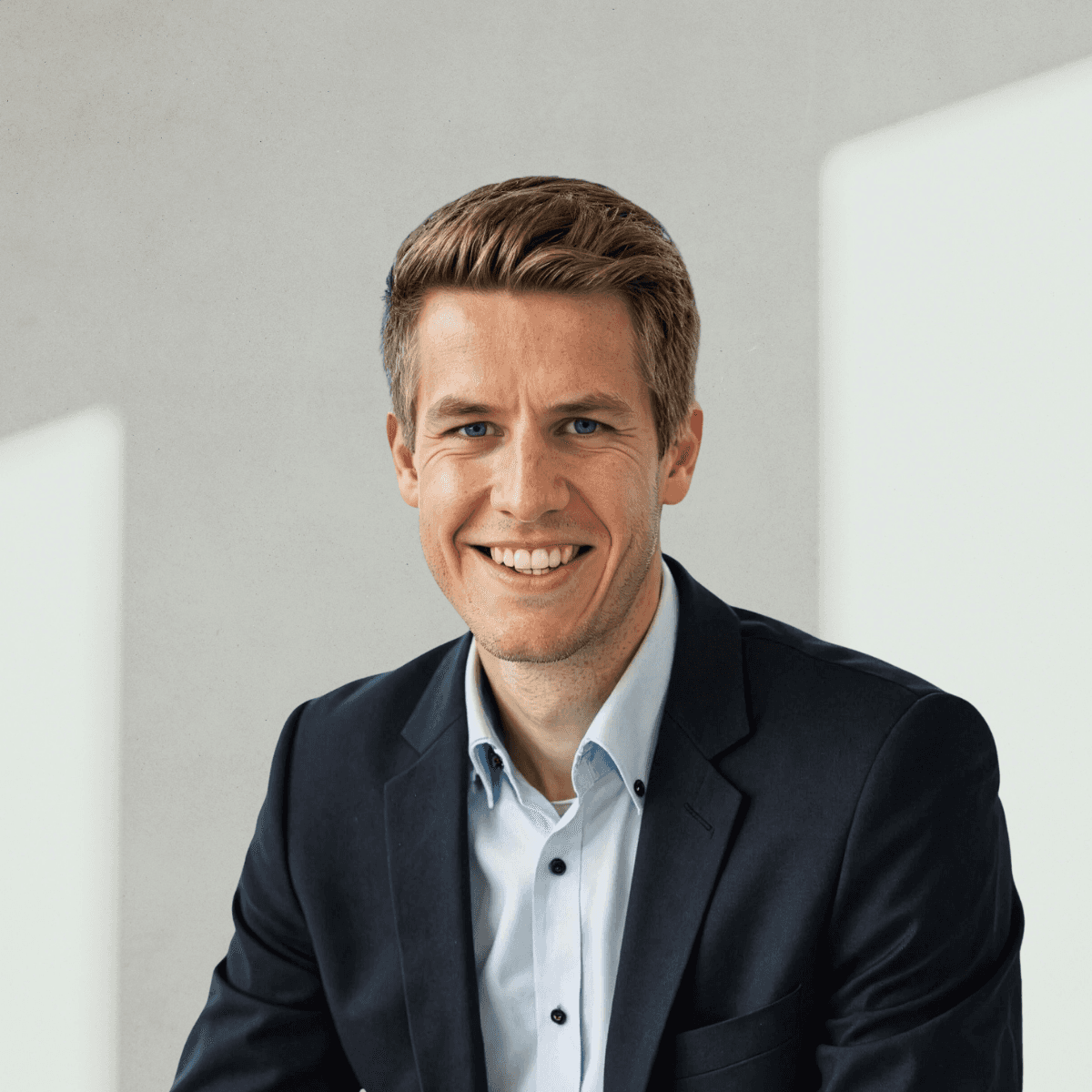Smiling young woman with curly hair sitting at a laptop, in front of a teal wall.