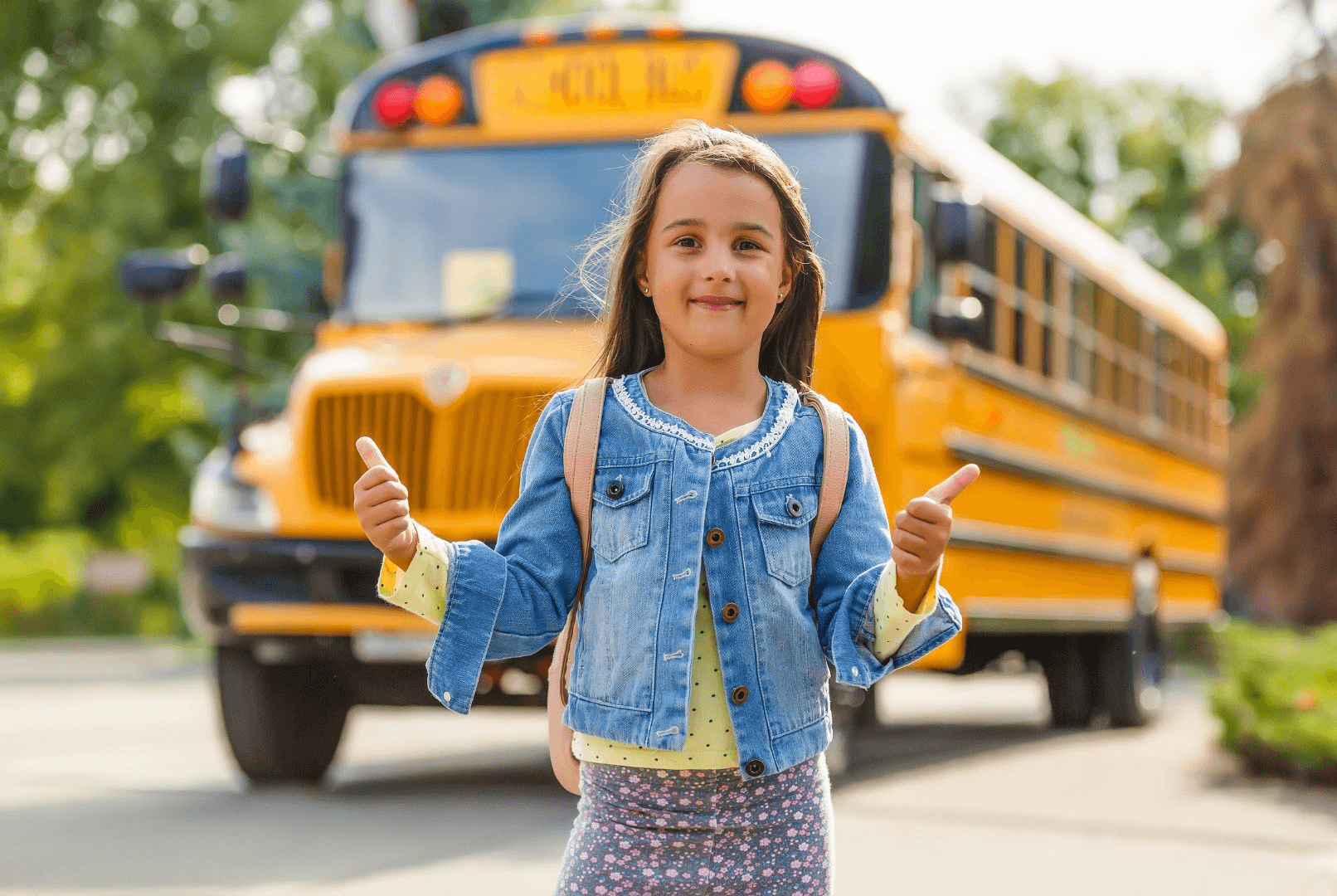 A girl giving a thumbs up in front of a school bus