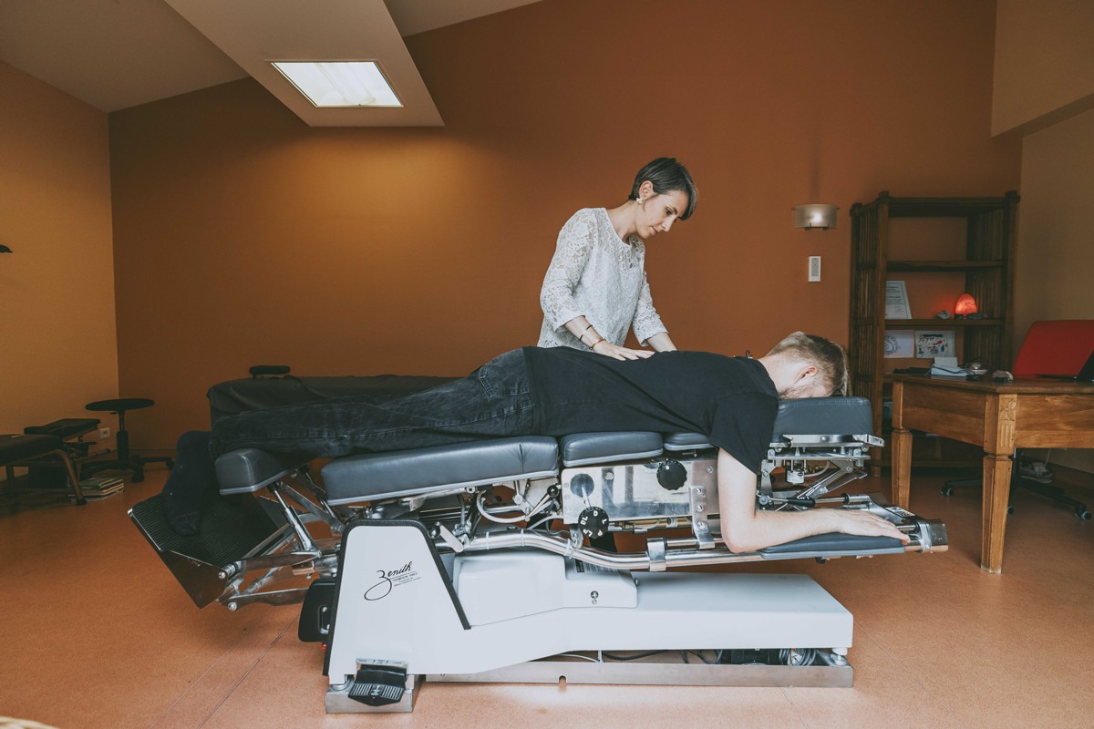 Mahiltde Hérault-Moreau, chiropracteur, effectuant un ajustement dorsal sur un patient allongé sur une table chiropratique spécialisée, visant à corriger l’alignement spinal et à soulager les douleurs dorsales.