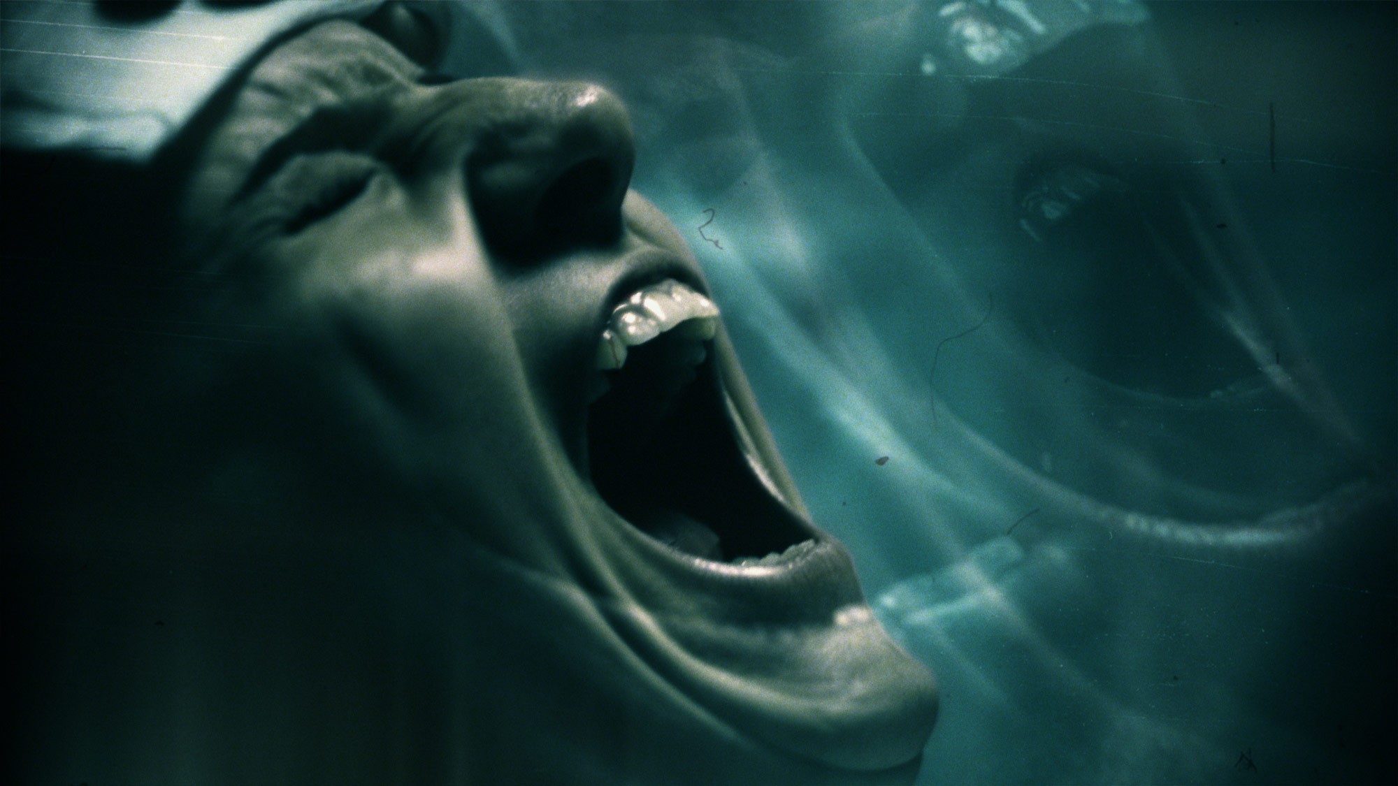 A woman screams with a distorted repetition effect layered over the top in a grim greenish hue, creating an unsettling and eerie visual from American Horror Stories.