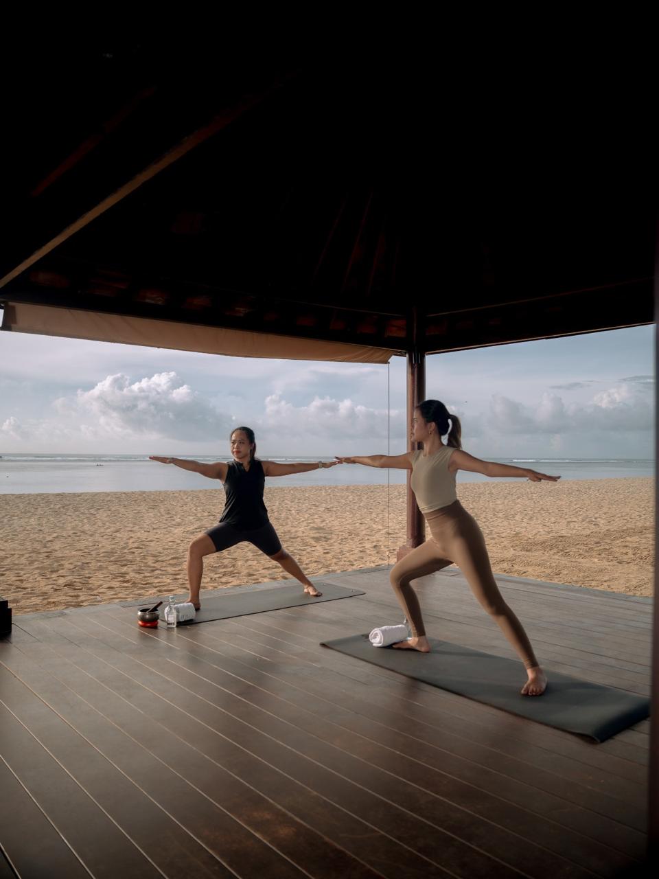 Group yoga class practicing warrior pose in a spacious studio overlooking mountains and sea views.