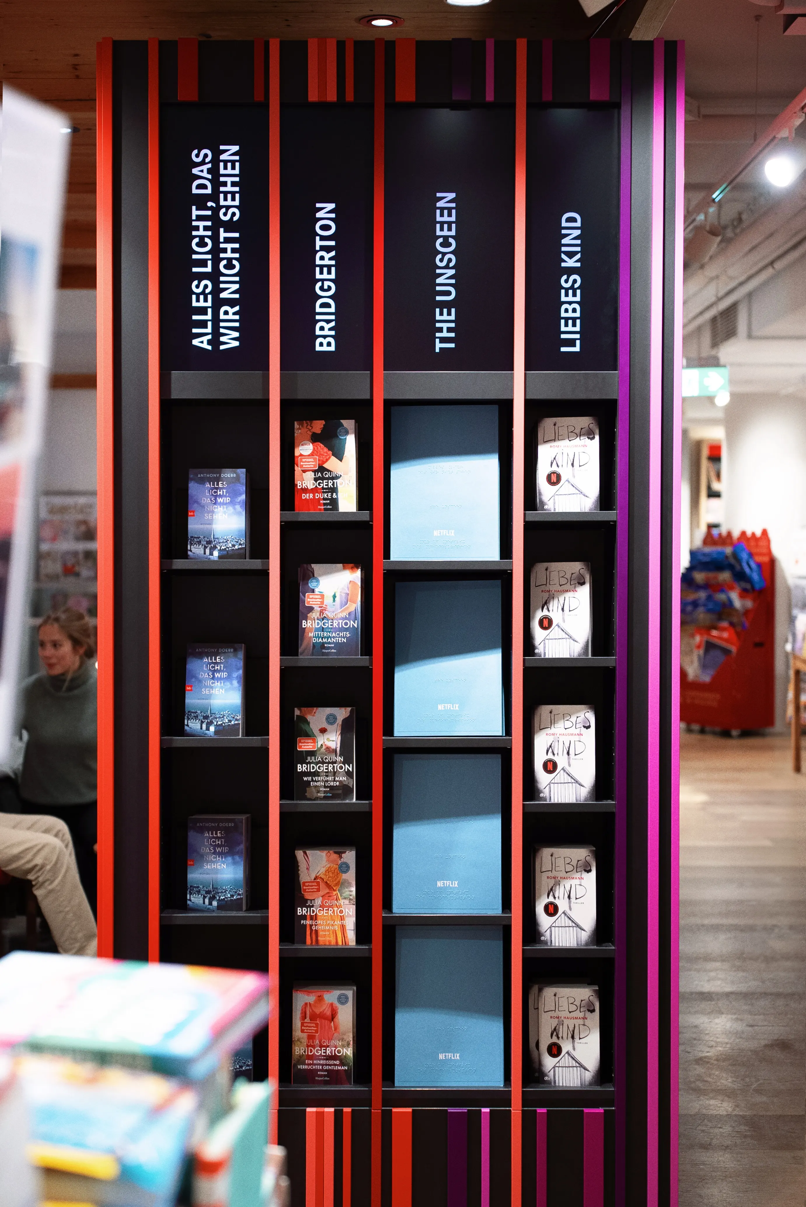 Book display of the NETFLIX TOWER with shelves for the series tie-in titles Alles Licht das wir nicht sehen, Bridgerton, The Unscreen and Liebes Kind, framed by red and purple stripes.