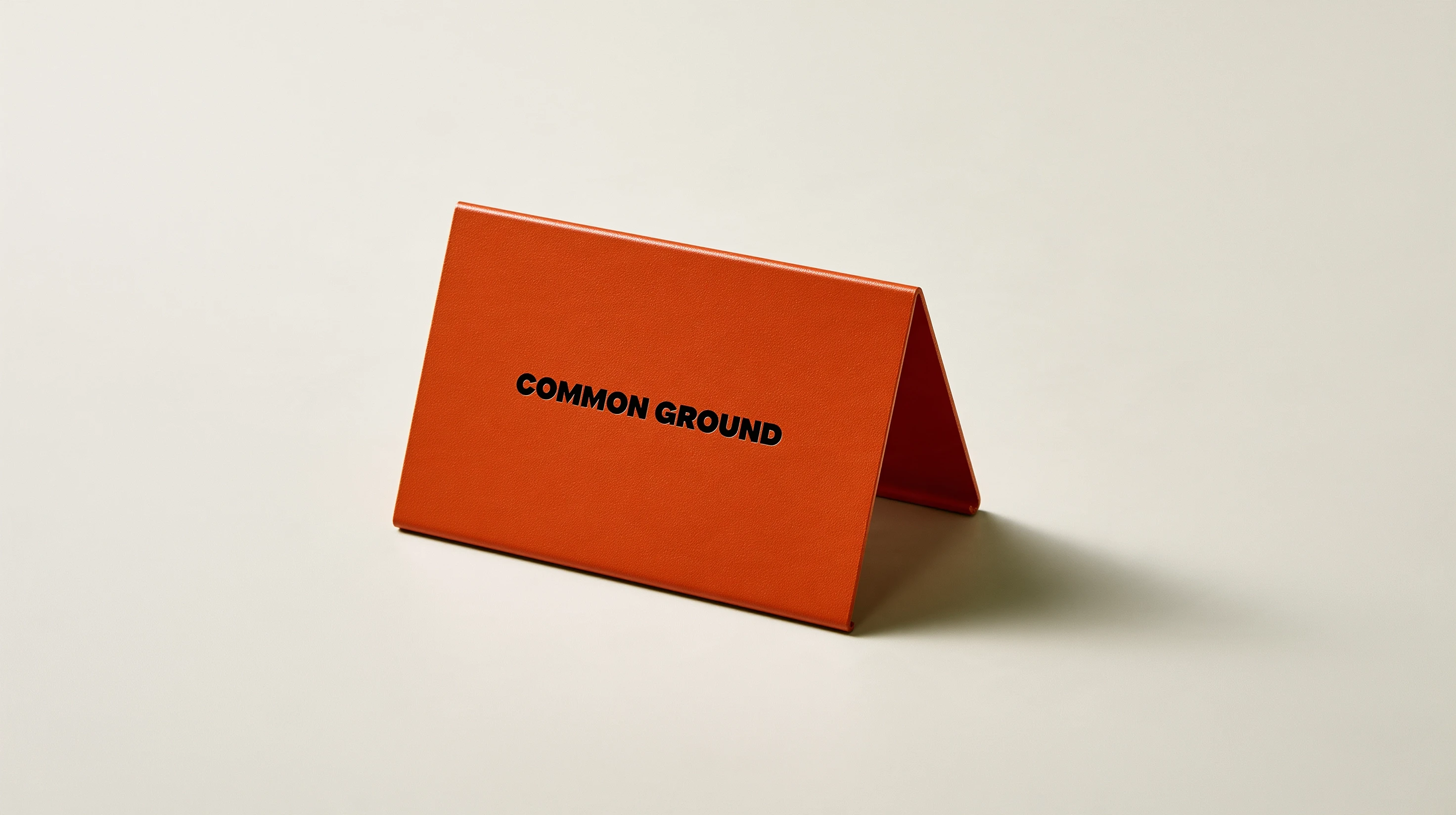 Orange Common Ground tabletop sign with a black wordmark on an off-white surface.