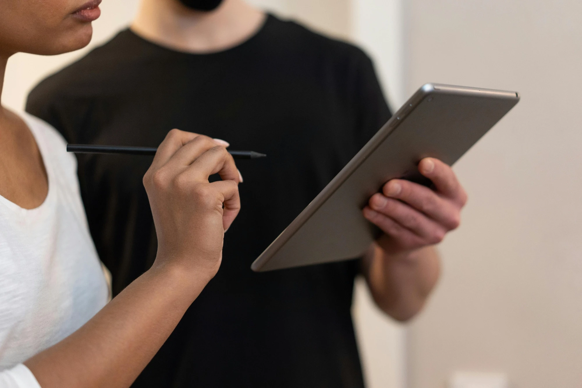 Two people collaborate using a digital tablet and stylus. One holds the tablet while the other gestures with the stylus, focusing intently.