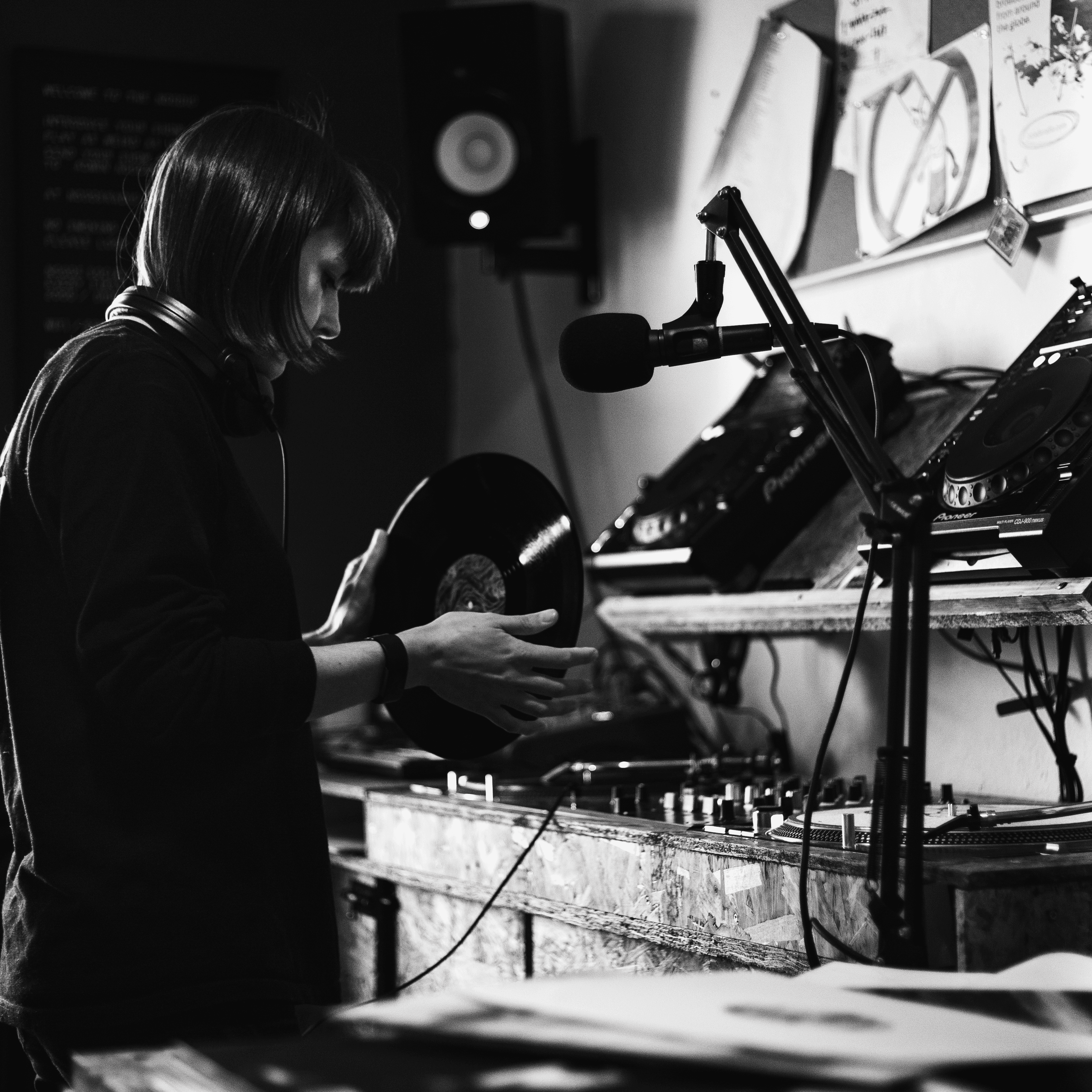 Woman holding vinyl record stood in front of dj equipment at Noods radio station