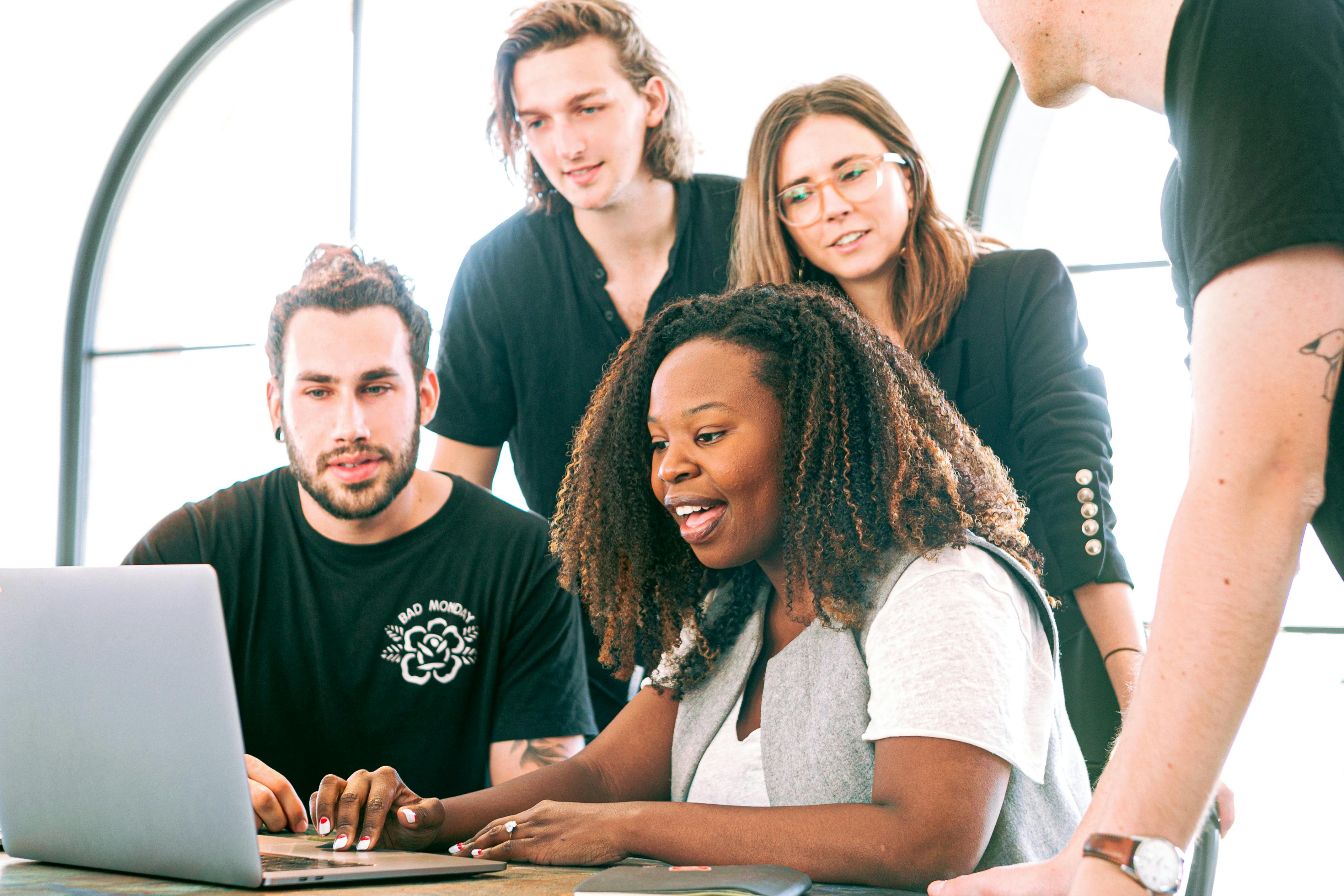 A group of four people collaboratively working on a laptop in a bright, modern workspace.