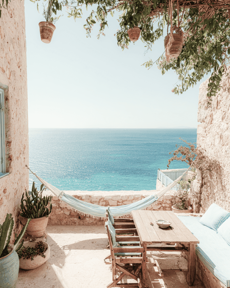Charming seaside patio with hammock, wooden seating, and ocean view.