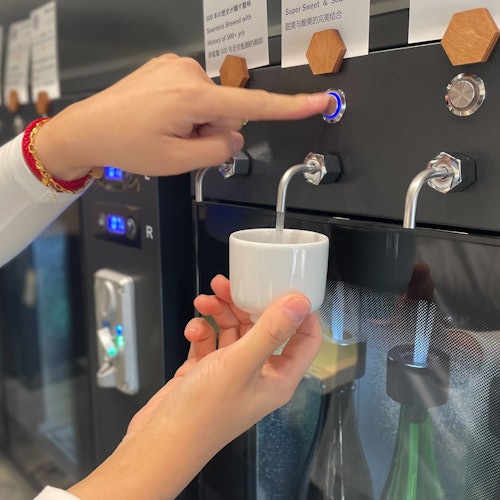 一個人從一部機器中將飲料倒入一個白色杯子，按下一個藍色燈光的按鈕。塑料瓶部分可見在下面。