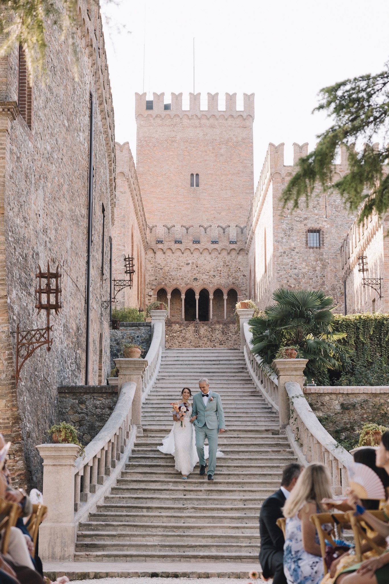 Sposi scendono la scalinata del Castello di Tabiano tra gli ospiti, reportage di matrimonio in Toscana