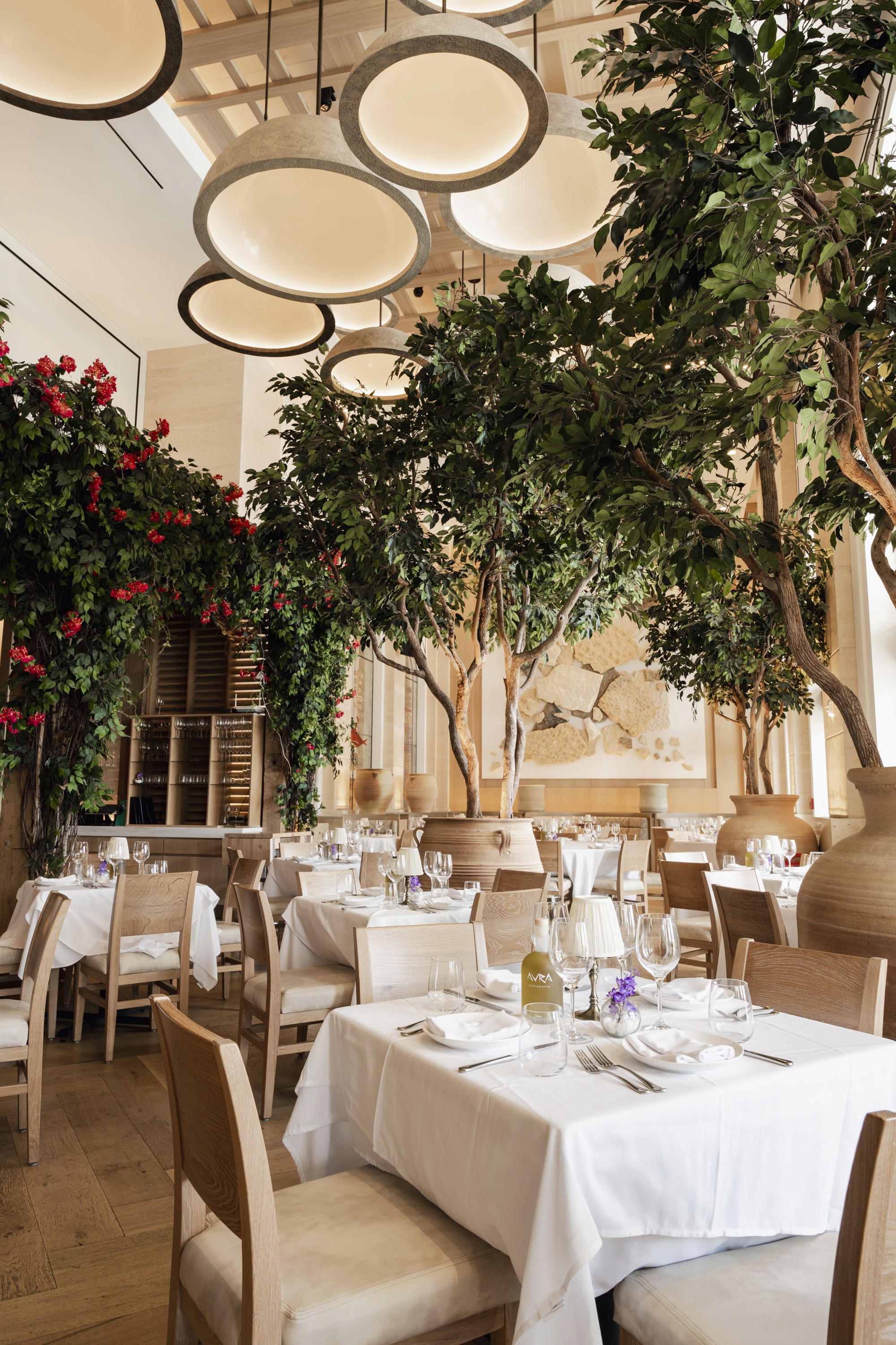 Elegant restaurant interior with green plants, circular light fixtures, and tables set for dining.
