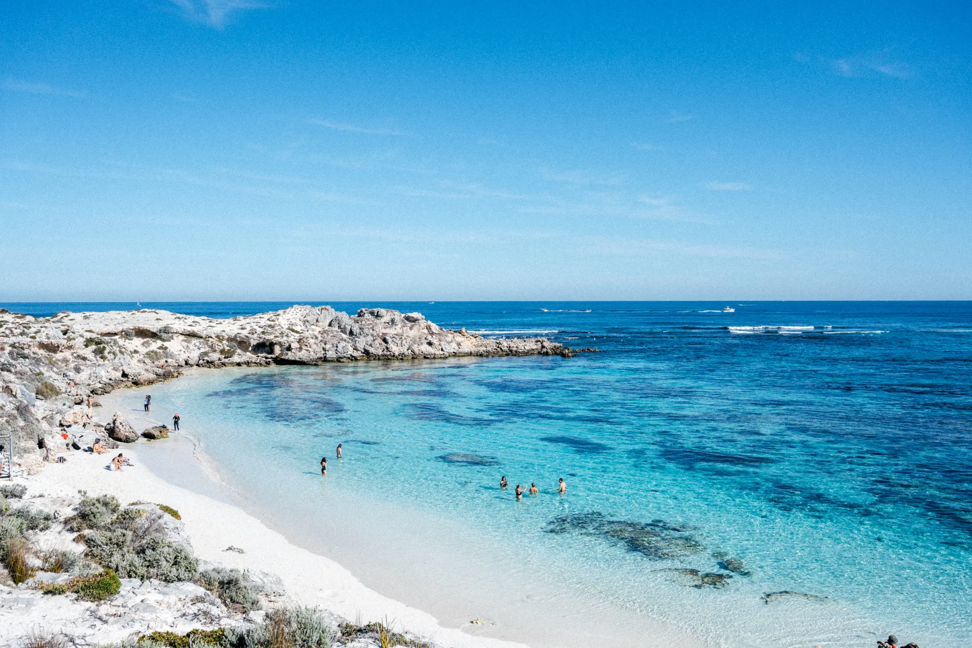 A small sheltered beach between limestone rocks with people swimming in clear water
