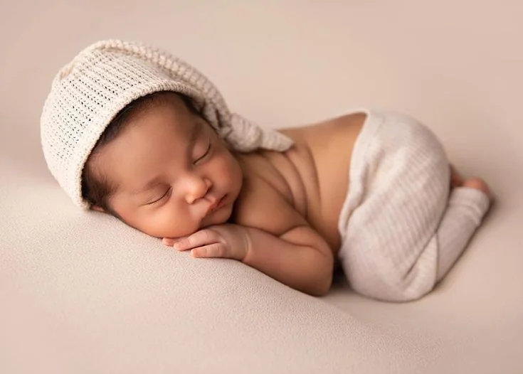 Sleeping newborn in a cream bonnet and wrap