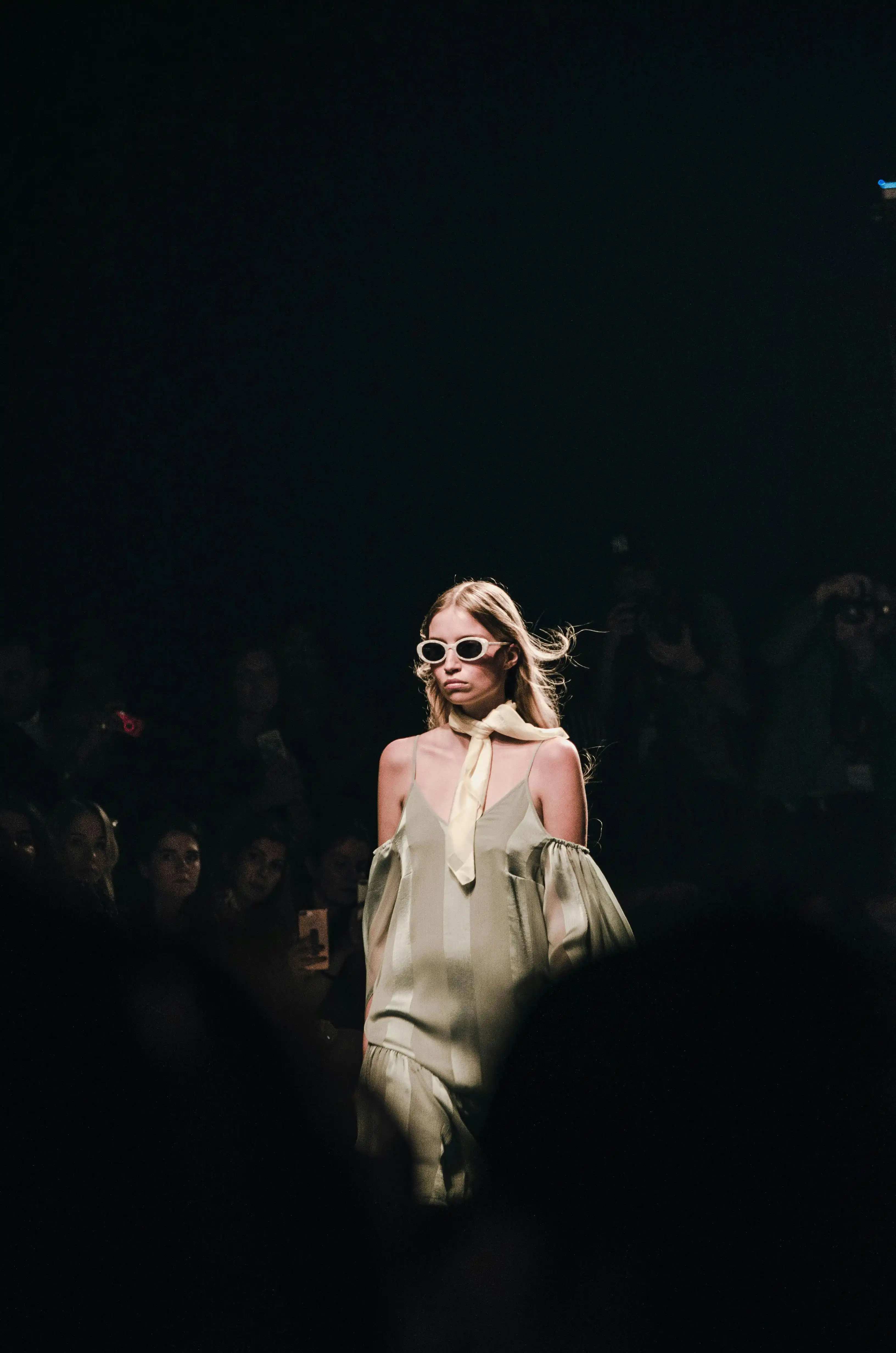 Model wearing beige dress walking on a runway.