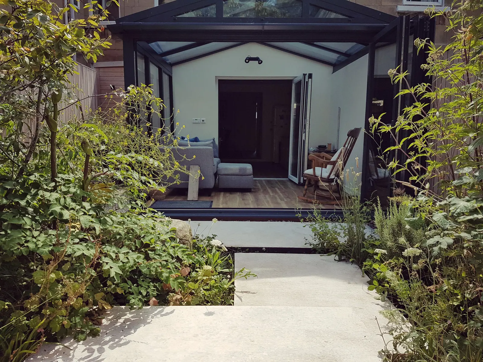 A modern entrance with wooden paneling, surrounded by greenery and a stone pathway leading to the door.