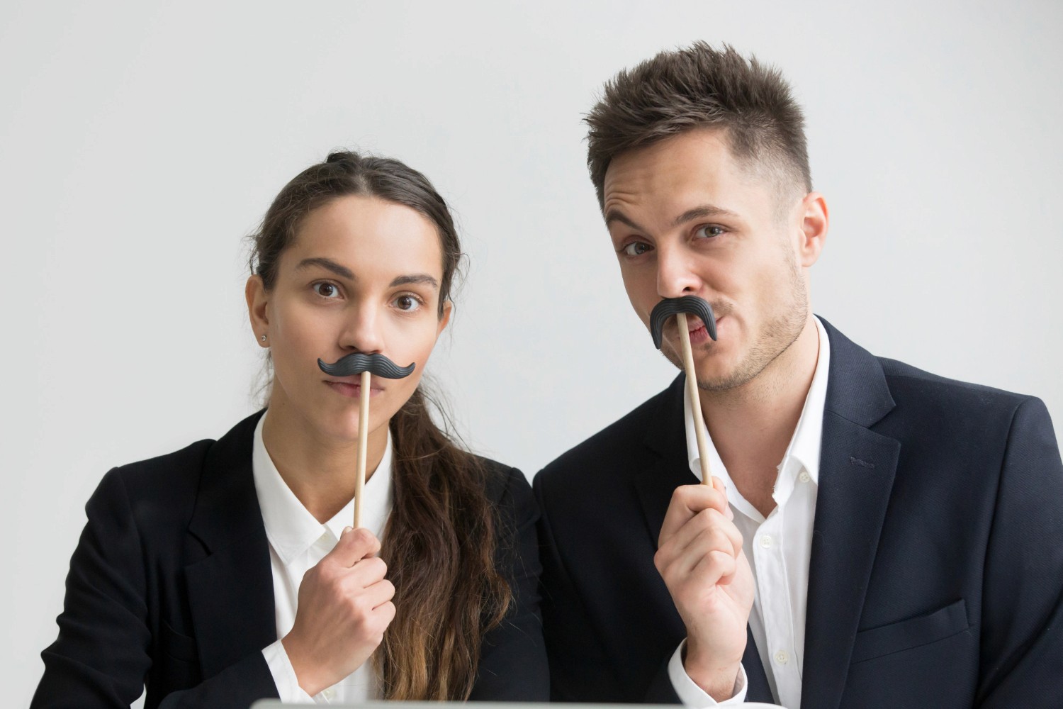 2 collègues posent devant un photobooth avec des fausses moustaches