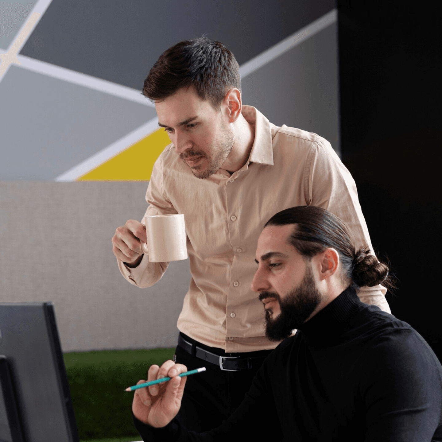 Two people collaborating at a desk, one pointing at a computer screen with a pen