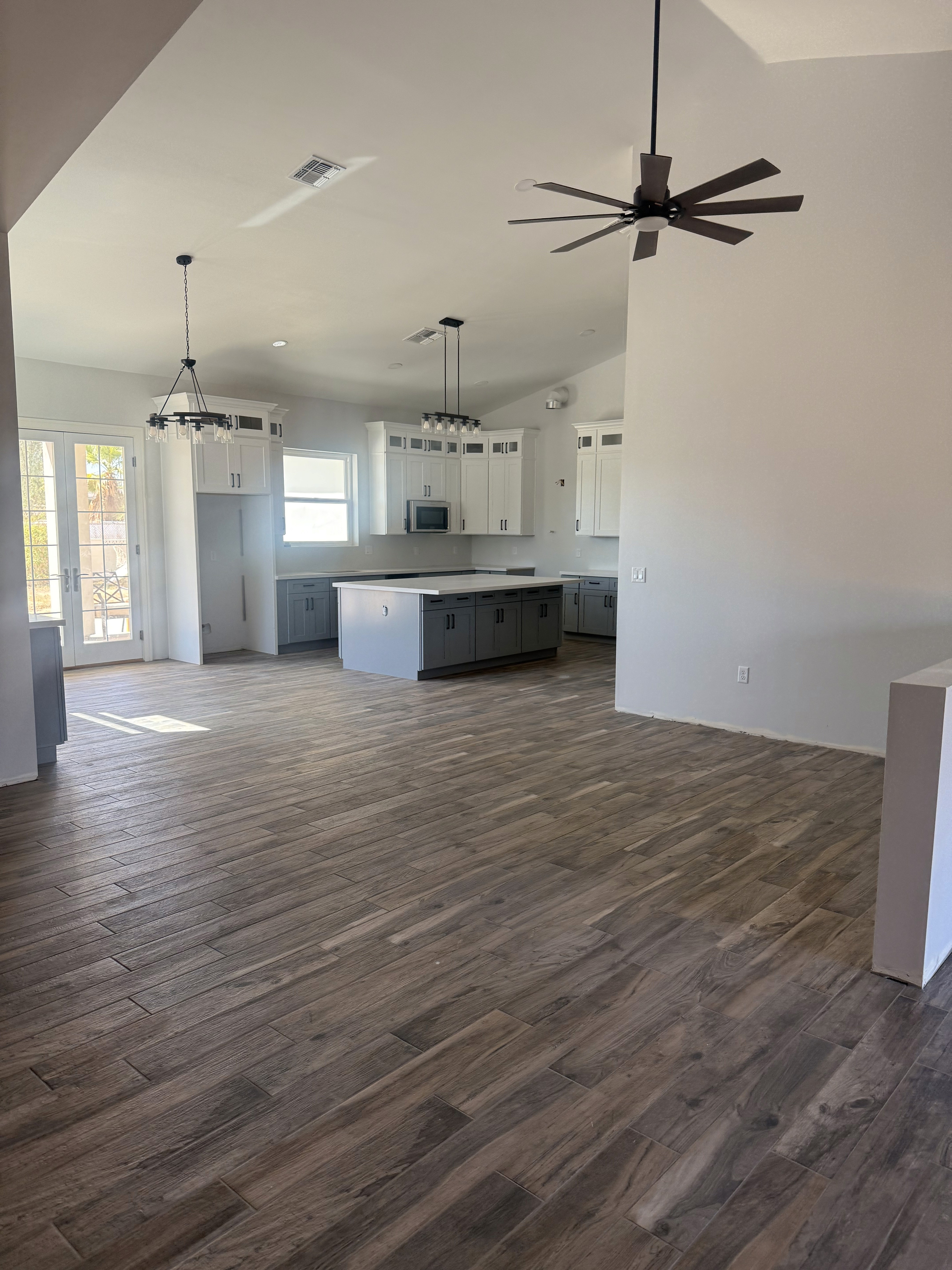 Modern open-plan living area with gray wood-look tile flooring, kitchen island, and pendant lights in a new home under construction.