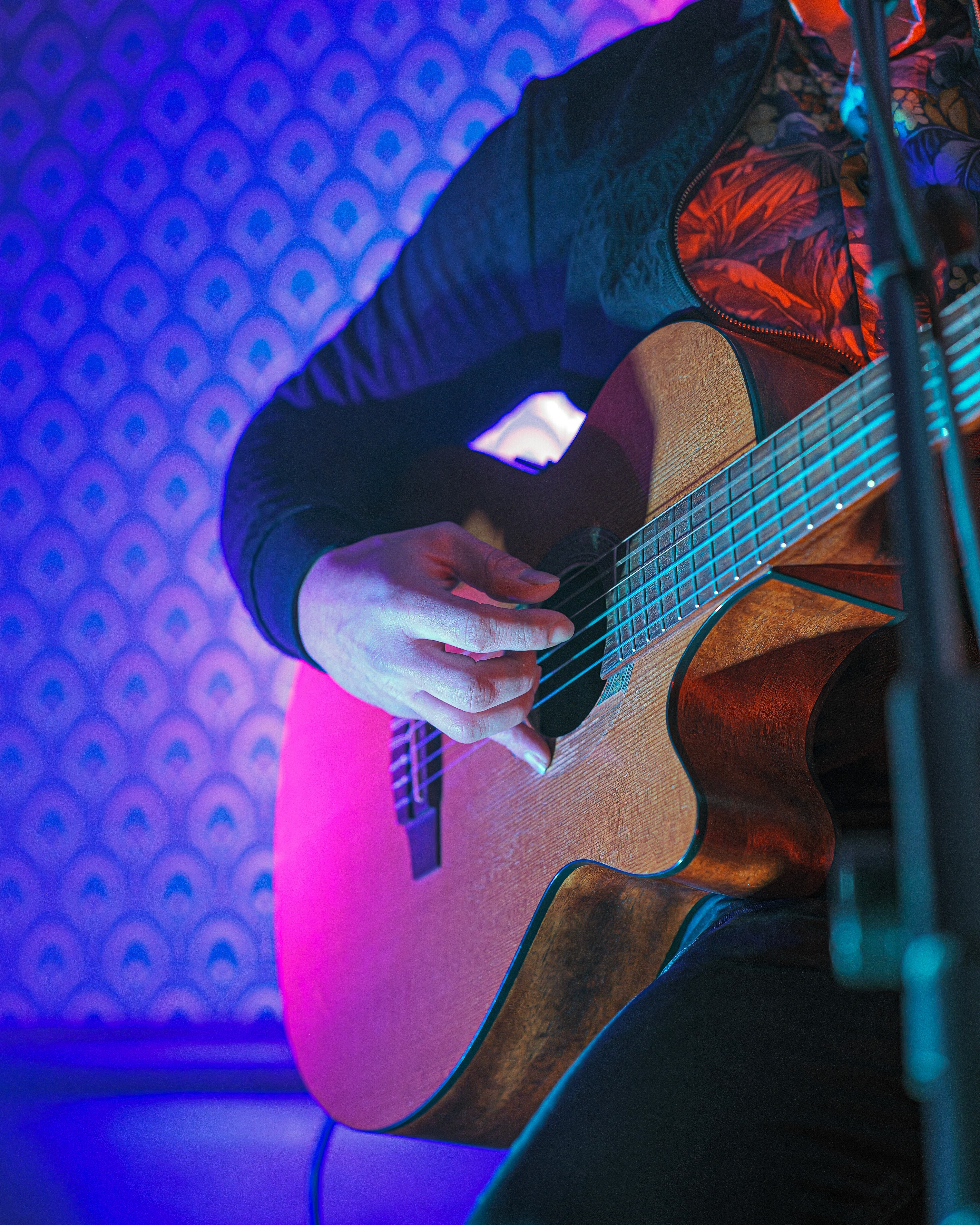A woman in a white blouse and dark vest sits on a park bench, looking away and smiling. A ukulele rests next to her.