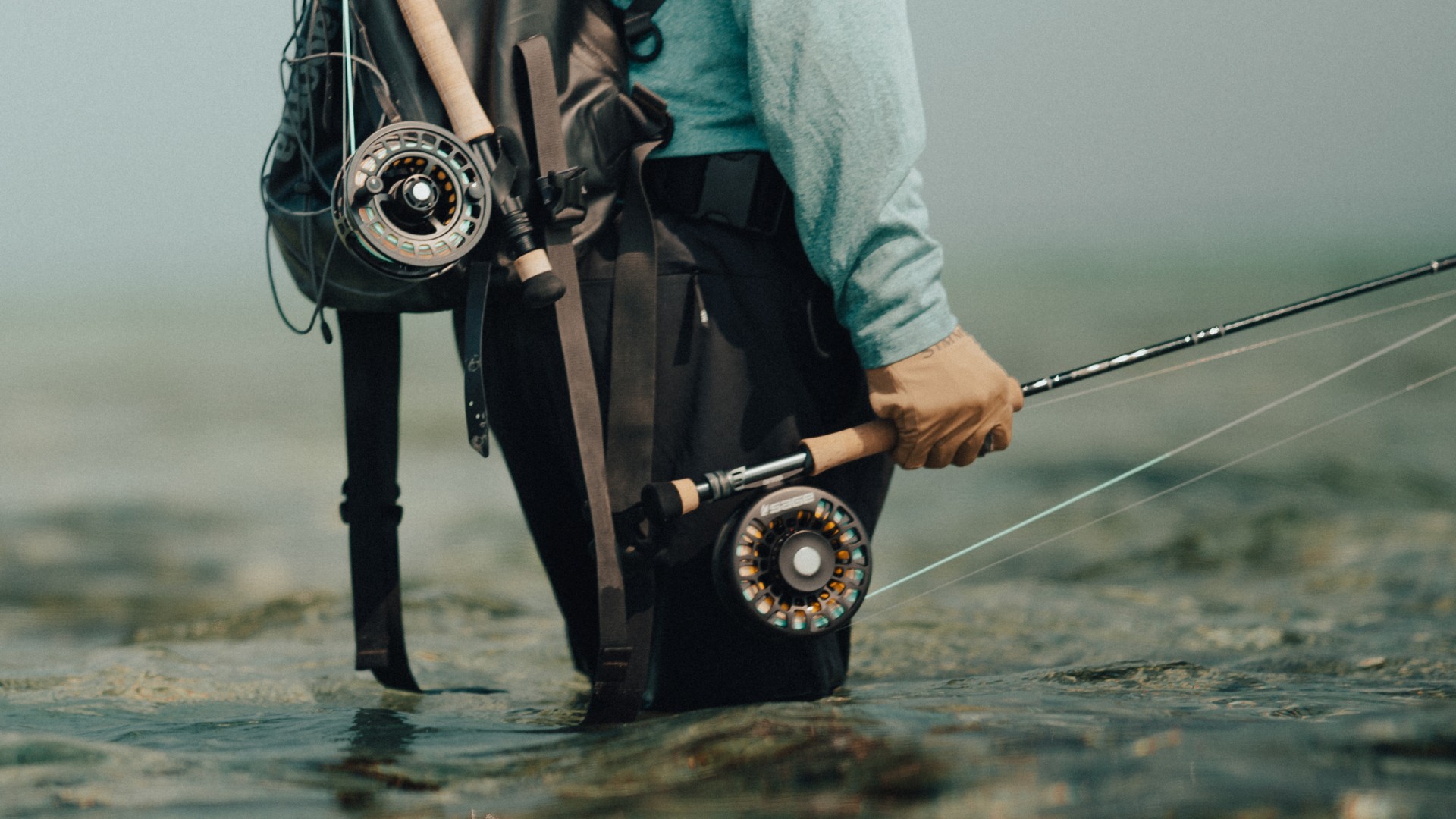 Angler with backpack and two fly fishing rods, standing knee deep on a Belizian pancake flat