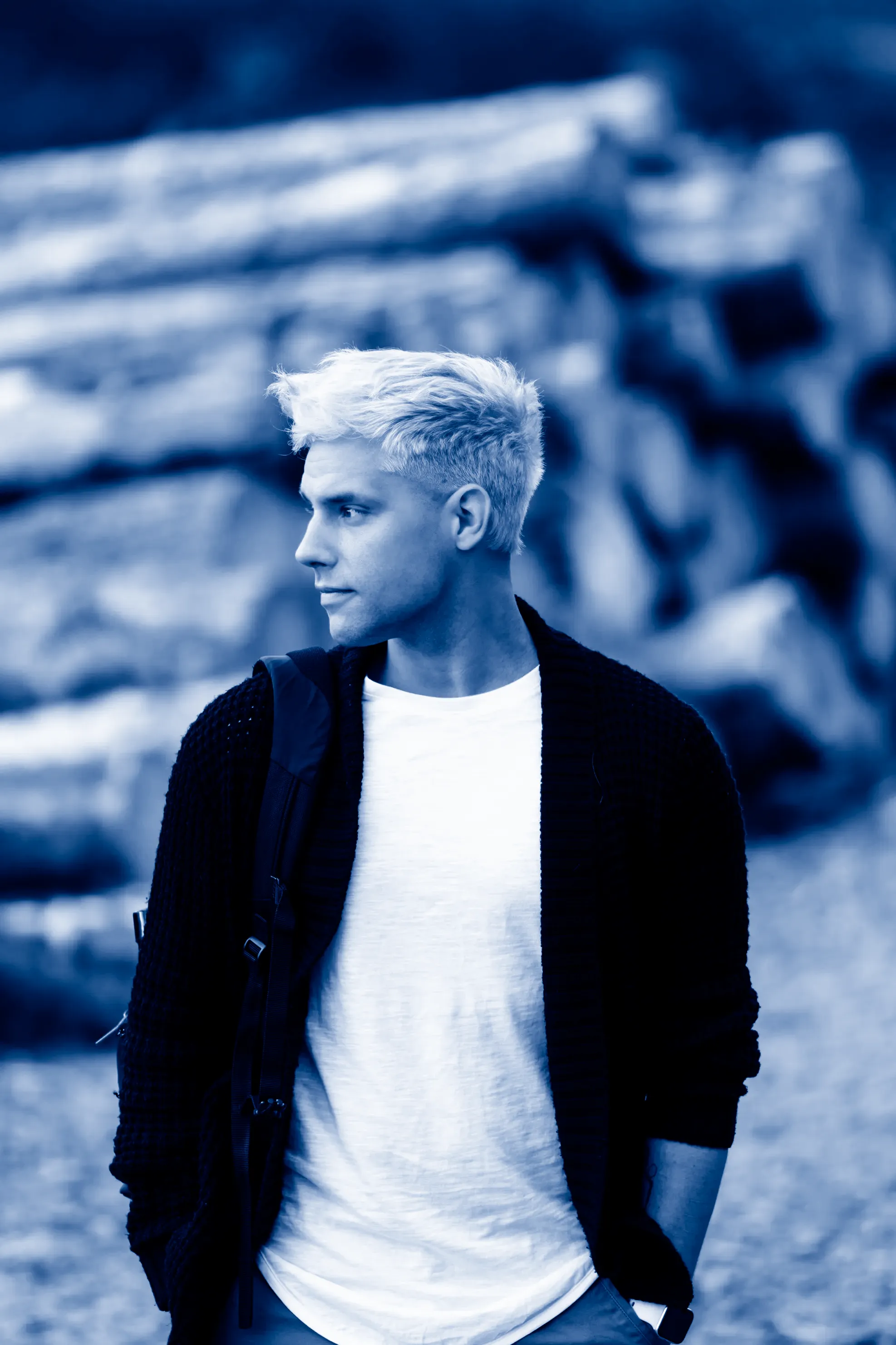 A young man with dark blue and white skin tones, wearing a black cardigan and having white hair.