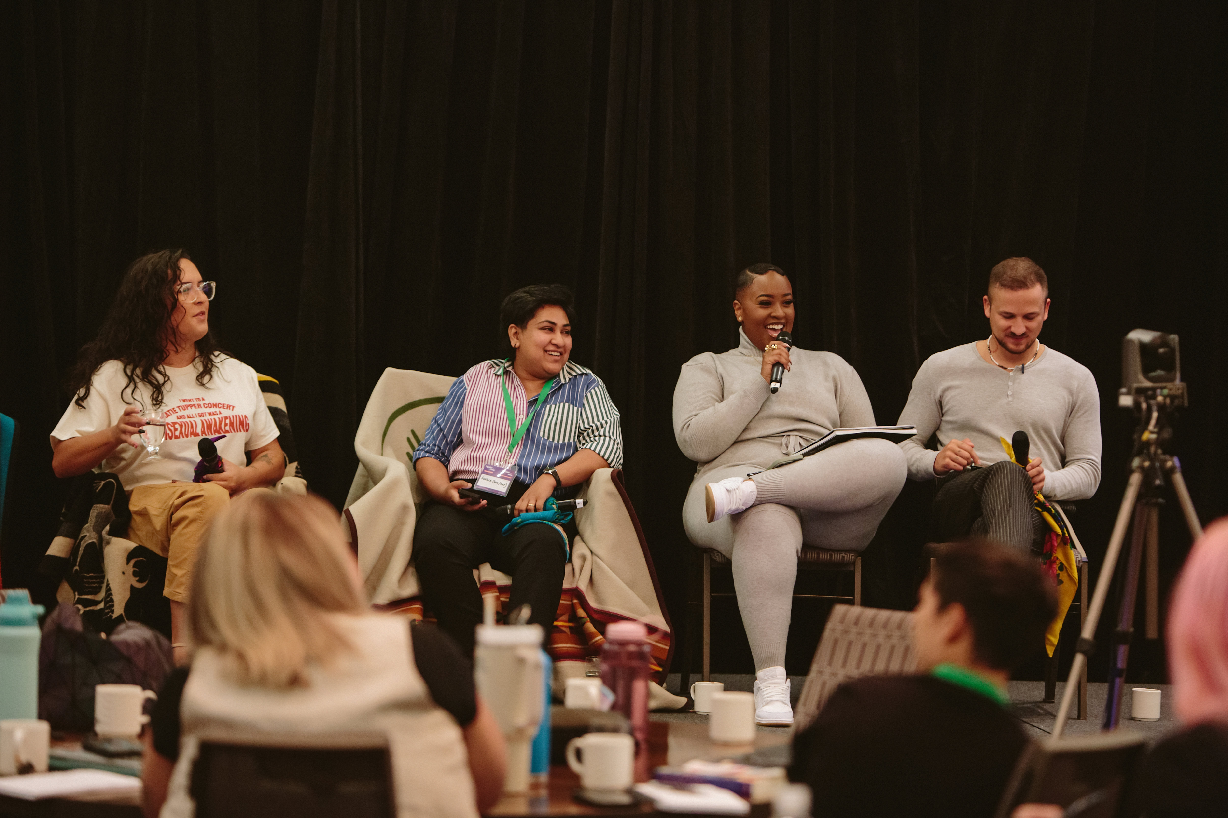 A panel discussion featuring four speakers seated on a stage, with an audience in the foreground.