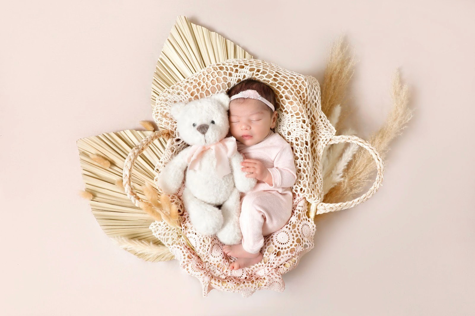 Baby sleeping next to a white teddy bear in a bohemian-style basket.