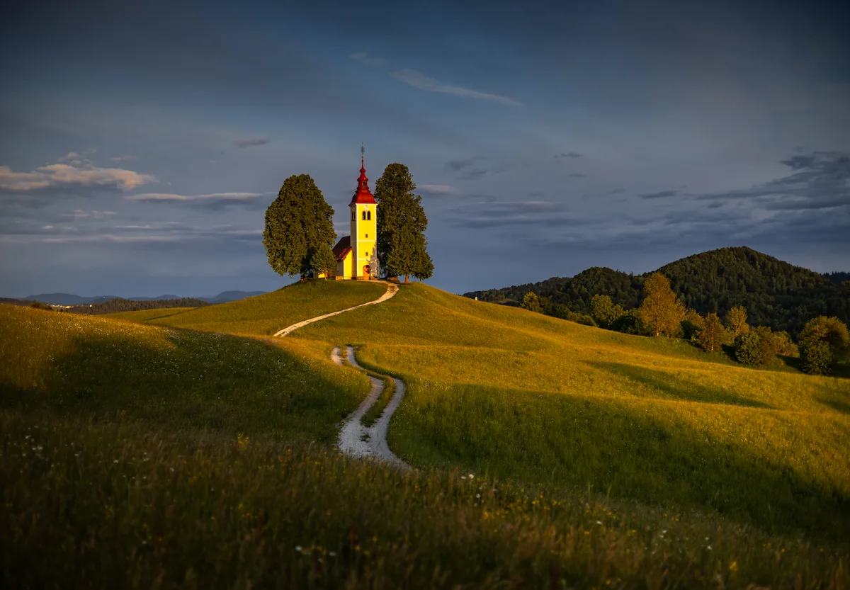 Sveti Tomaž Church at Vrsnik during sunset, with a winding road leading up through the grassy fields.